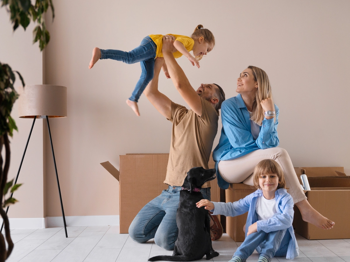 Familie fericită, alături de câine, mutându-se într-o nouă locuință, simbolizând protecția și confortul oferite de asigurarea locuinței